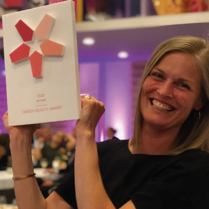 En smilende kvinde fra det danske hold, der holder en skønhedspris i hånden ved Danish Beauty Awards 2021.