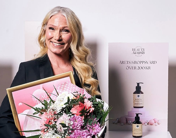 En kvinde, der holder en buket blomster og en pris, og smiler i et festligt øjeblik.