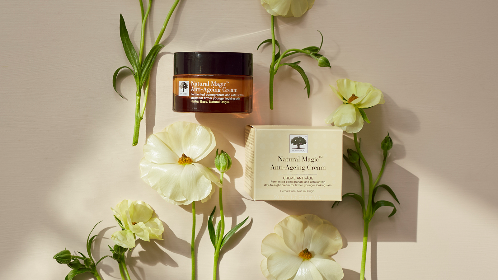 Natural Magic™ Anti-Ageing Cream med krukke og æske omgivet af lyse blomster på lys baggrund.