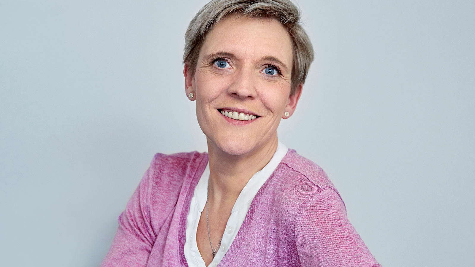 Smilende kvinde med kort hår ser direkte ind i kameraet mod en lys baggrund.