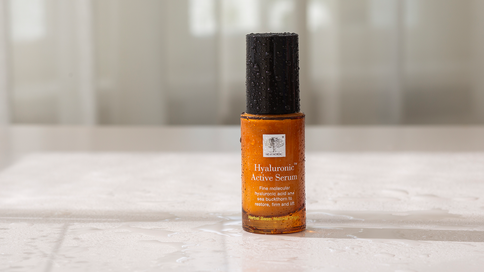 New Nordic Hyaluronic Active Serum™ i ravfarvet flaske med vanddråber på lys baggrund.