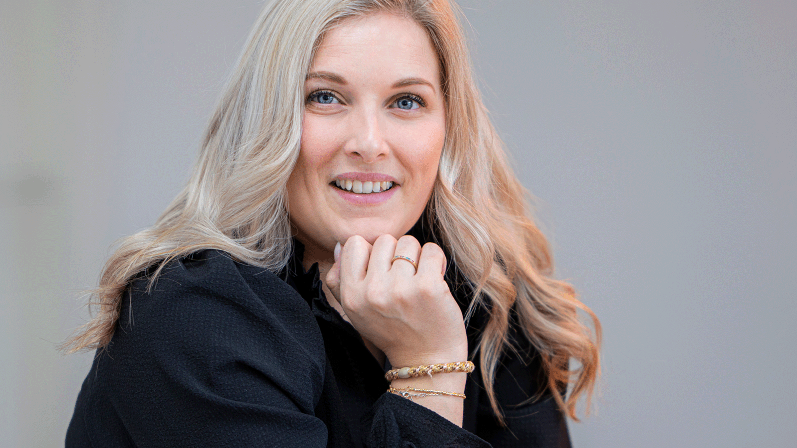 Hair Volume™ 15 Smilende kvinde med lyst hår ser direkte mod kameraet med hånden under hagen.