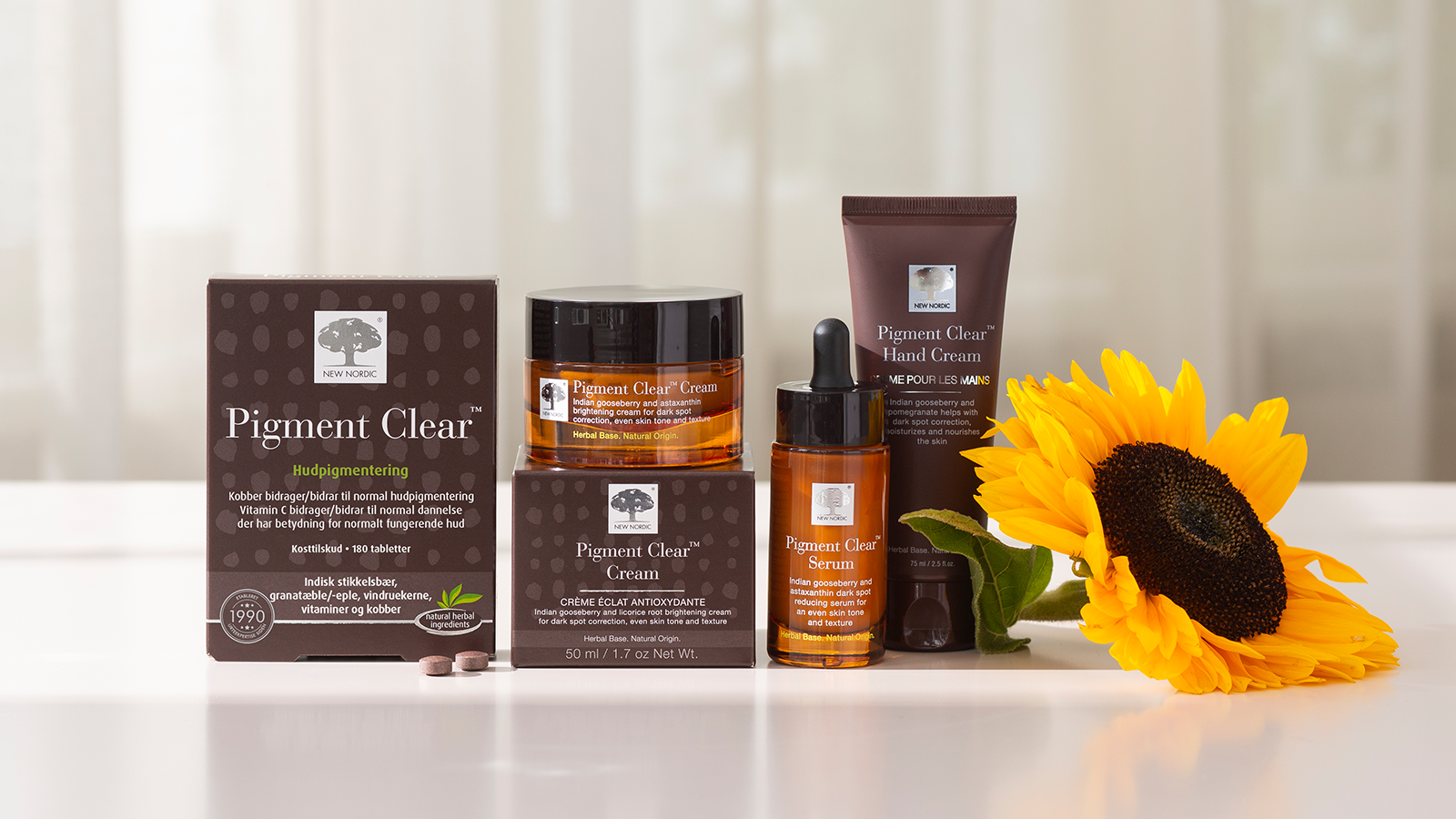 New Nordic Pigment Clear™ hudplejeserie med creme, serum, håndcreme og kosttilskud ved en solsikke.