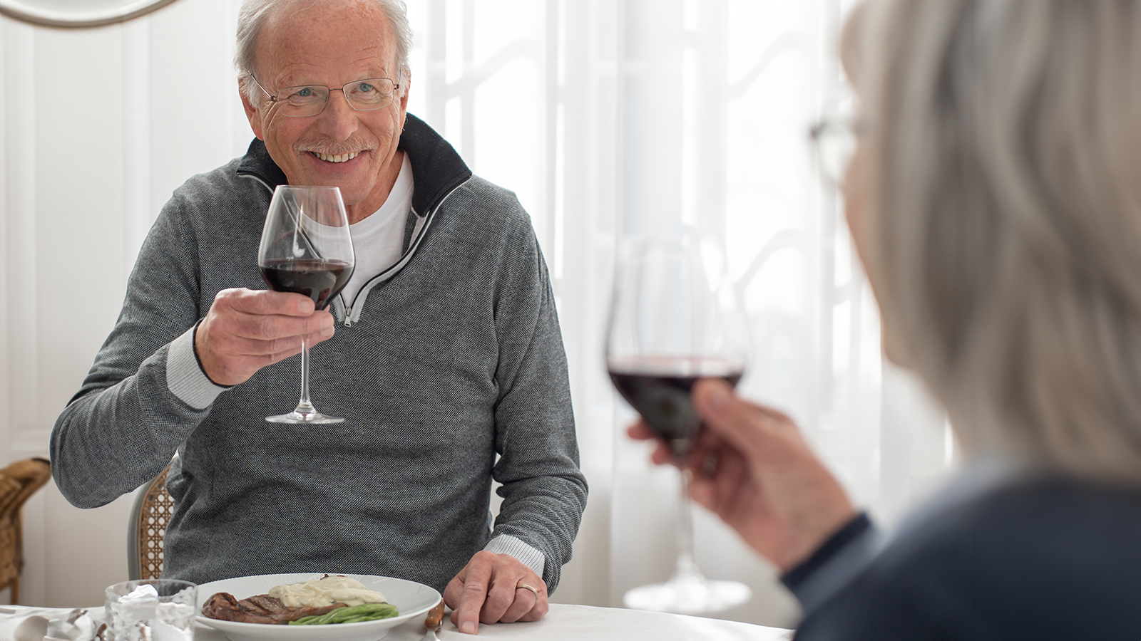 Forår = grillpølser og kold rosé 5 Ældre par skåler med rødvin over et måltid ved spisebordet.